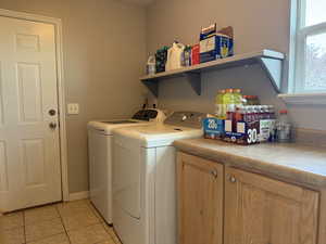 Laundry area with washing machine and dryer, light tile patterned floors, and cabinet space