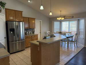 Kitchen featuring stainless steel fridge, tasteful backsplash, vaulted ceiling, hanging light fixtures, and a chandelier