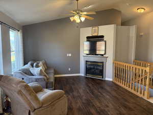 Living area featuring lofted ceiling, wood finished floors, a glass covered fireplace, and a ceiling fan