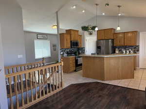Kitchen featuring appliances with stainless steel finishes, light countertops, brown cabinets, decorative backsplash, and lofted ceiling