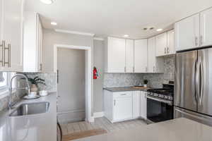 Kitchen with appliances with stainless steel finishes, white cabinetry, ornamental molding, backsplash, and recessed lighting