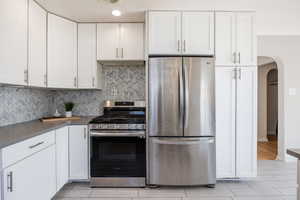 Kitchen with appliances with stainless steel finishes, arched walkways, backsplash, and white cabinetry