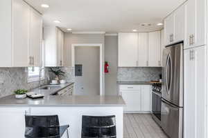 Kitchen with a peninsula, stainless steel appliances, white cabinetry, recessed lighting, and ornamental molding