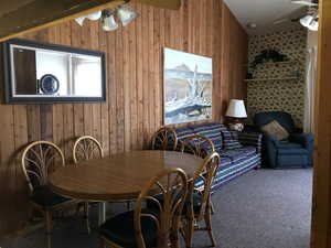 Carpeted dining area featuring ceiling fan and wood walls