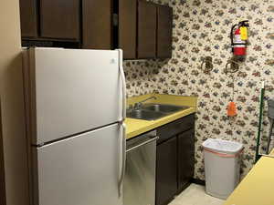Kitchen featuring freestanding refrigerator, wallpapered walls, light countertops, stainless steel dishwasher, and light floors