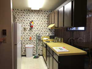 Kitchen featuring wallpapered walls,  appliances, light countertops, and under cabinet range hood