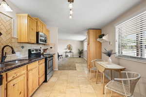Kitchen with appliances with stainless steel finishes, backsplash, dark stone countertops, and light carpet