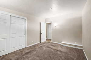 Unfurnished bedroom with carpet floors, a textured ceiling, and a closet