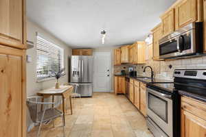 Kitchen with appliances with stainless steel finishes, backsplash, light brown cabinetry, and a textured ceiling