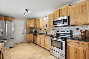 Kitchen with stainless steel appliances, backsplash, dark stone countertops, and light tile patterned floors