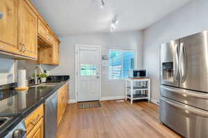 Kitchen featuring appliances with stainless steel finishes, lofted ceiling, light wood-style flooring, dark stone countertops, and a textured ceiling