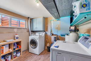 Laundry room with washer and dryer, light wood-type flooring, and cabinet space