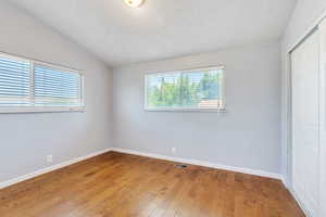 Unfurnished bedroom featuring a closet, lofted ceiling, a textured ceiling, and light wood-style floors