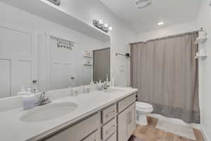 Bathroom with double vanity, wood finished floors, shower / bath combination with curtain, and recessed lighting