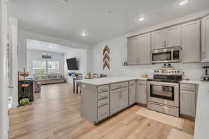 Kitchen with stainless steel appliances, gray cabinets, a peninsula, light wood-type flooring, and light countertops