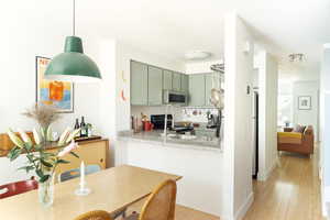 Kitchen with green cabinets, light countertops, electric stove, stainless steel microwave, and light wood-style flooring