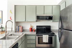 Kitchen with green cabinets, appliances with stainless steel finishes, and tile counters