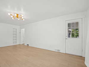 Empty room with a chandelier, built in features, and light wood-type flooring