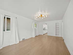 Unfurnished living room with a chandelier, light wood finished floors, and built in shelves