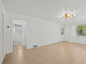 Empty room featuring a chandelier, light wood-style floors, and a textured ceiling