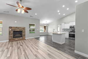 Kitchen with open floor plan, vaulted ceiling, appliances with stainless steel finishes, white cabinetry, and recessed lighting