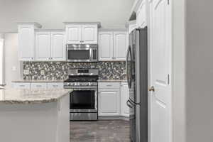 Kitchen with appliances with stainless steel finishes, backsplash, white cabinetry, and light stone countertops
