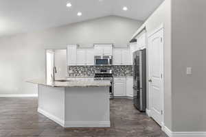 Kitchen featuring stainless steel appliances, lofted ceiling, backsplash, white cabinetry, and light stone counters