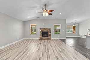 Unfurnished living room with a stone fireplace, light wood finished floors, a ceiling fan, vaulted ceiling, and a chandelier