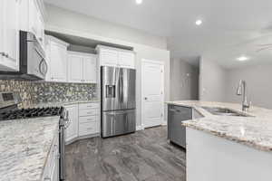 Kitchen featuring appliances with stainless steel finishes, white cabinetry, tasteful backsplash, dark marble finish flooring, and light stone counters