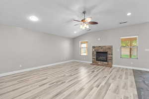 Unfurnished living room featuring ceiling fan, healthy amount of natural light, a fireplace, light wood-style floors, and vaulted ceiling