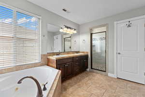 Full bathroom featuring a tub with jets, a shower stall, plenty of natural light, and double vanity