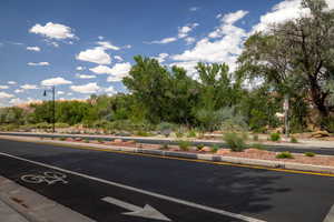 View of asphalt street featuring street lights, curbs, view of wooded area, and sidewalks