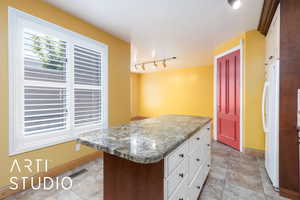 Kitchen with white cabinetry, freestanding refrigerator, a kitchen island, light stone counters, and track lighting