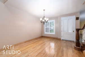 Spare room featuring stairs, light wood-style floors, and a chandelier