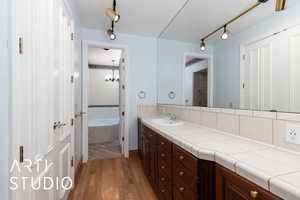 Full bath featuring vanity, a bath, wood finished floors, track lighting, and a chandelier