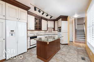 Kitchen featuring white appliances, a kitchen island, light stone countertops, glass insert cabinets, and light tile patterned floors