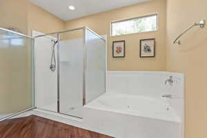 Full bath with a stall shower, a garden tub, and wood finished floors