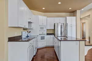 Kitchen featuring dark countertops, white appliances, dark wood-style floors, recessed lighting, and white cabinets