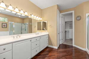 Bathroom with wood finished floors, a shower stall, double vanity, and a spacious closet