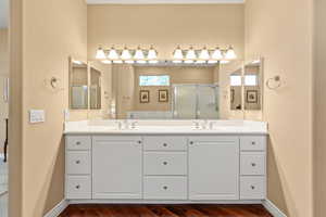 Bathroom featuring a shower stall, double vanity, and wood finished floors