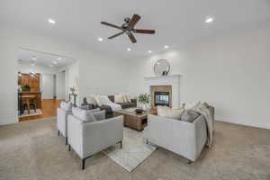 Living room featuring recessed lighting, light colored carpet, ceiling fan, crown molding, and a tiled fireplace