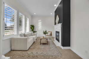 Living room with healthy amount of natural light, ornamental molding, a fireplace with flush hearth, recessed lighting, and light carpet