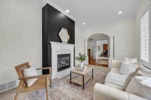 Living area featuring arched walkways, crown molding, ornate columns, a brick fireplace, and wood finished floors