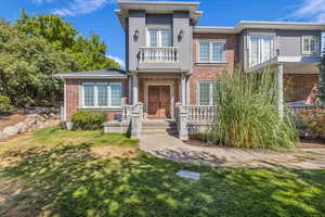 View of front of property featuring a front lawn, brick siding, and a balcony