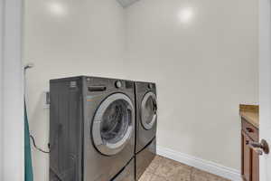 Laundry area featuring separate washer and dryer, light tile patterned floors, and cabinet space