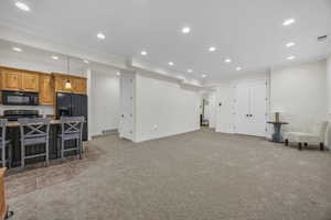 Kitchen featuring ornamental molding, a breakfast bar, black appliances, recessed lighting, and light colored carpet
