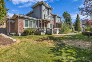 View of front of house with a balcony, brick siding, and a front lawn