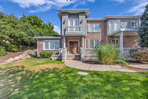 View of front of home with a balcony, a front yard, and brick siding