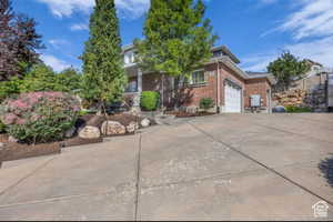 View of property hidden behind natural elements with brick siding, driveway, and an attached garage