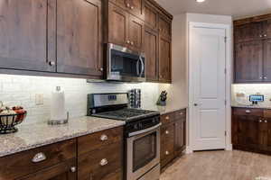 Kitchen with appliances with stainless steel finishes, decorative backsplash, light stone countertops, dark brown cabinetry, and light wood-type flooring